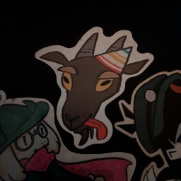 A sticker of a goat head, in a party hat, sticking its tongue out. Under it is a ralsei sticker.
