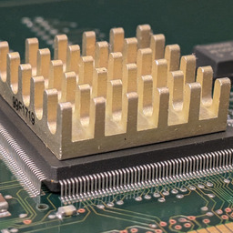 a close-up of a brass heatsink on a microchip on a circuit board. gold contacts are visible at the bottom of the frame