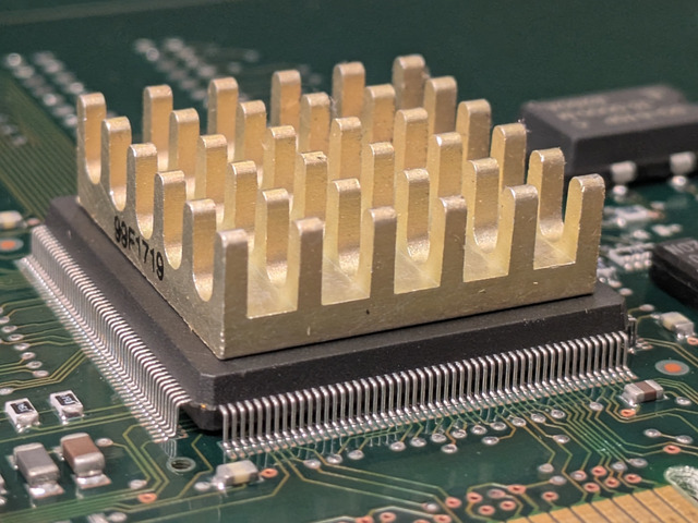 a close-up of a brass heatsink on a microchip on a circuit board. gold contacts are visible at the bottom of the frame